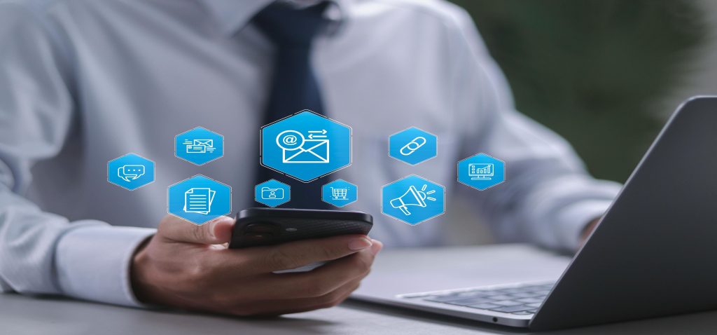 Profissional a utilizar um celular com ícones digitais flutuantes de e-mail, marketing e vendas, simbolizando a comunicação e as ferramentas da gestão comercial.