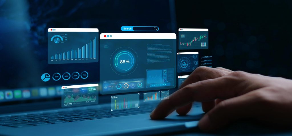 Mão a utilizar um portátil com ecrãs digitais flutuantes que mostram gráficos e análises de dados, ilustrando a prática tecnológica em Análise e Desenvolvimento de Sistemas: conheça mais este curso.