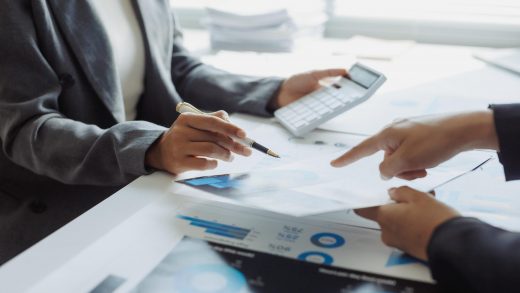 Pessoas analisando relatórios e usando calculadora sobre a mesa. Habilidades desenvolvidas no curso de gestão financeira.